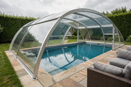 Abri de piscine rétractable en polycarbonate installé sur une piscine résidentielle avec terrasse en pierre et jardin paysager