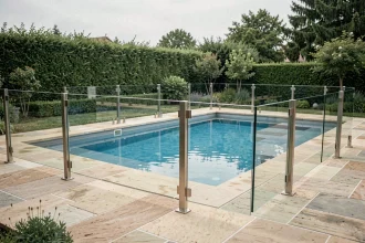 Barrière de piscine en verre transparent discrète autour d'une piscine moderne avec terrasse en pierre naturelle