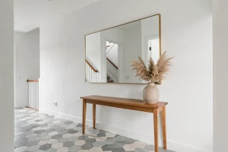 Grand miroir mural XXL à cadre laiton brossé dans une entrée avec console en bois et carreaux de ciment
