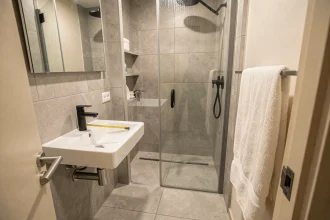 Petite salle de bain de 4 m² avec douche en verre, lavabo suspendu et carrelage gris clair, illustrant une organisation optimale de l'espace