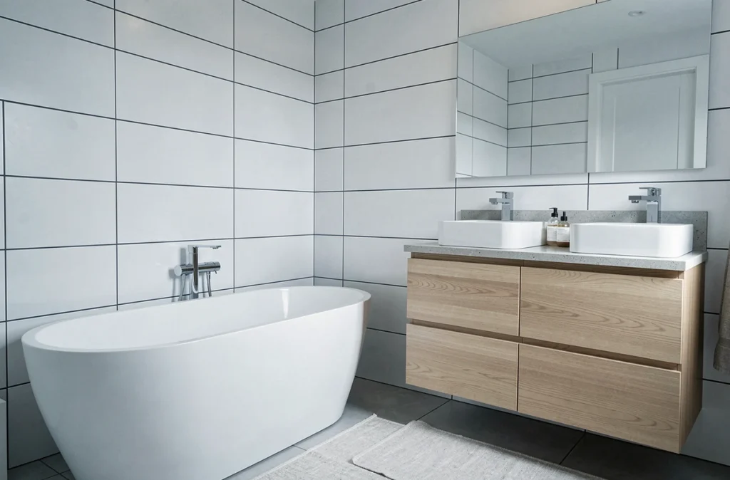 Salle de bain familiale de 7 m² avec baignoire îlot, double vasque en bois clair et carrelage blanc mat, montrant un espace confortable et bien dimensionné